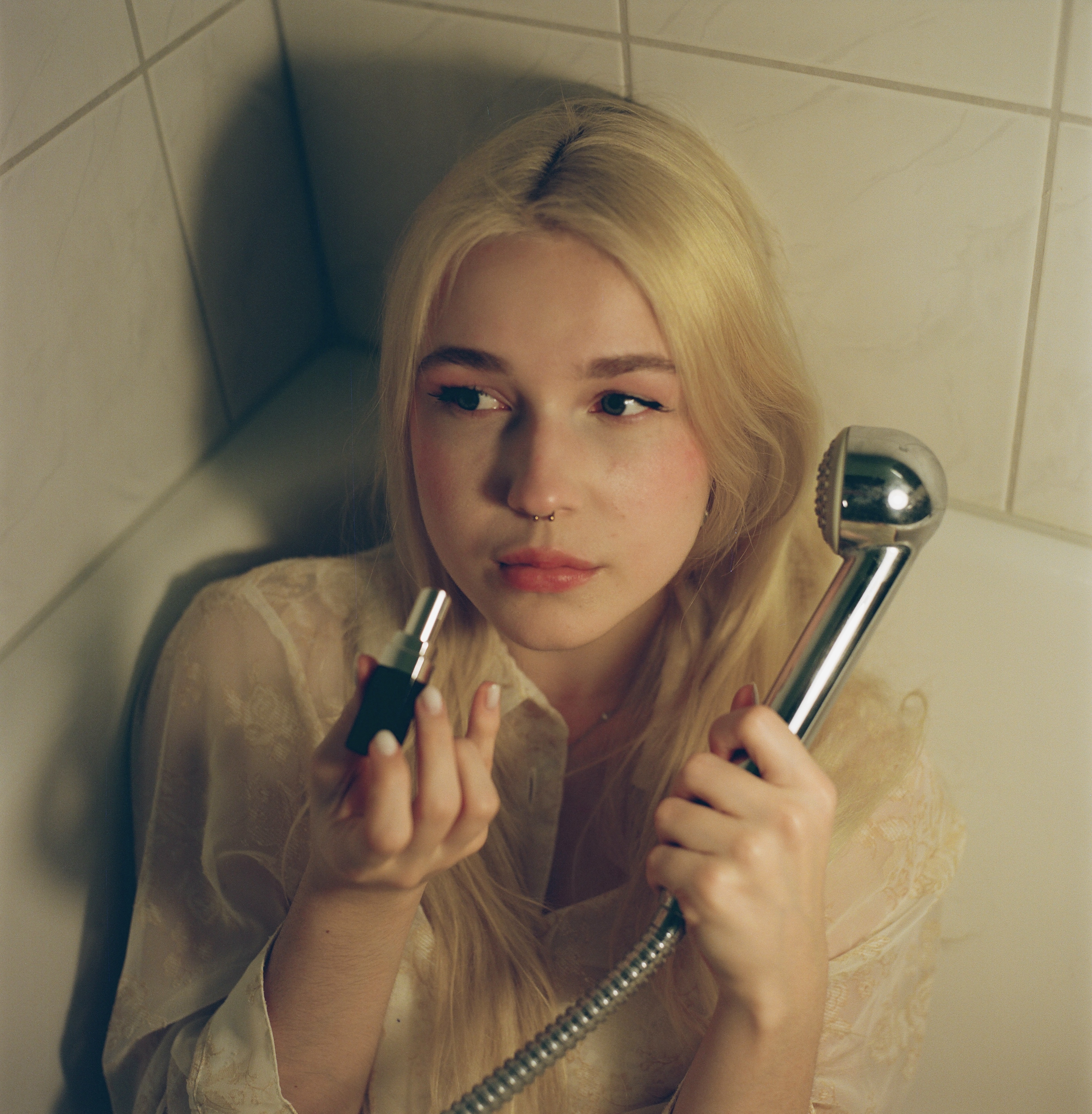 Maria in the bathtub corner, lipstick in one hand, shower head in the other