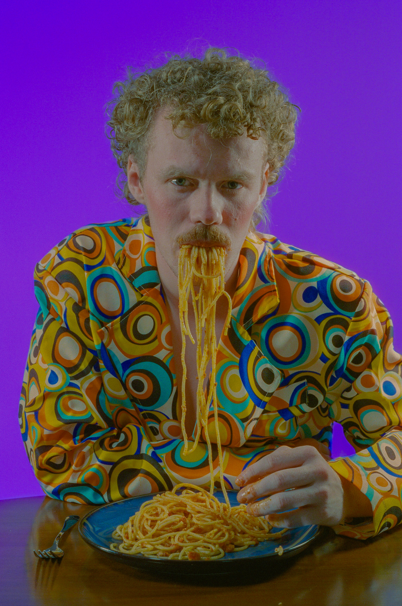Sindri at the table, spaghetti mid-bite, against a purple backdrop
